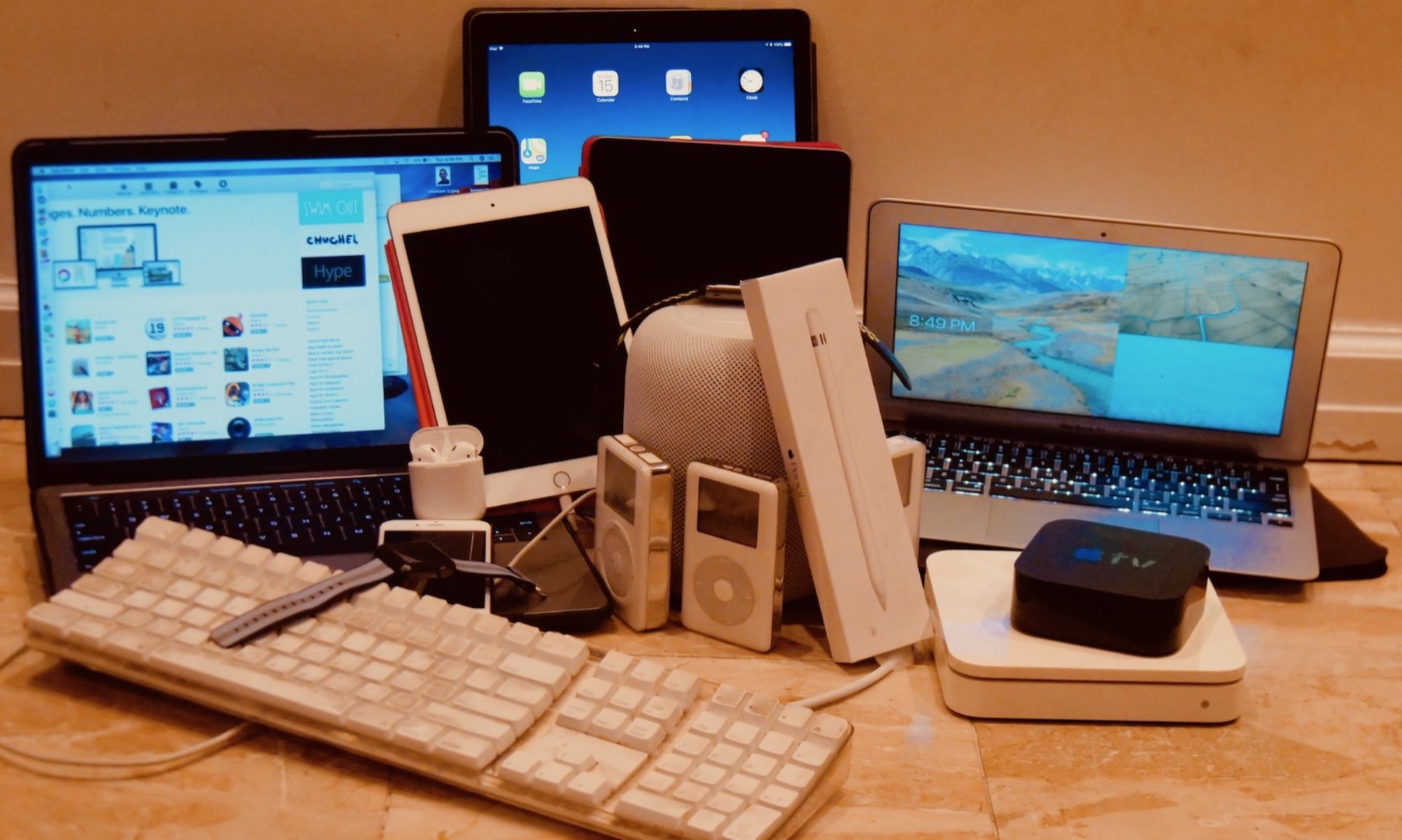A pile of Apple gear: MacBooks, iPads, iPods, a HomePod, an Apple TV and an old Apple keyboard